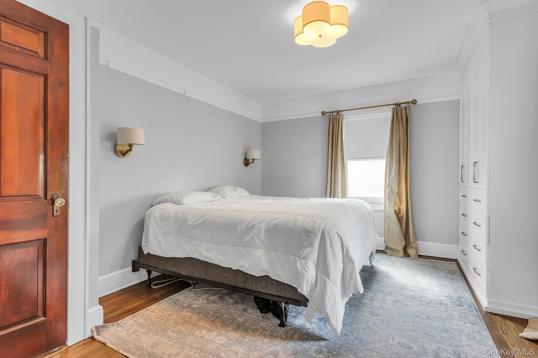 Hardwood flooring, crown molding, built-in cabinetry, two wall sconces, and a ceiling-mounted light fixture