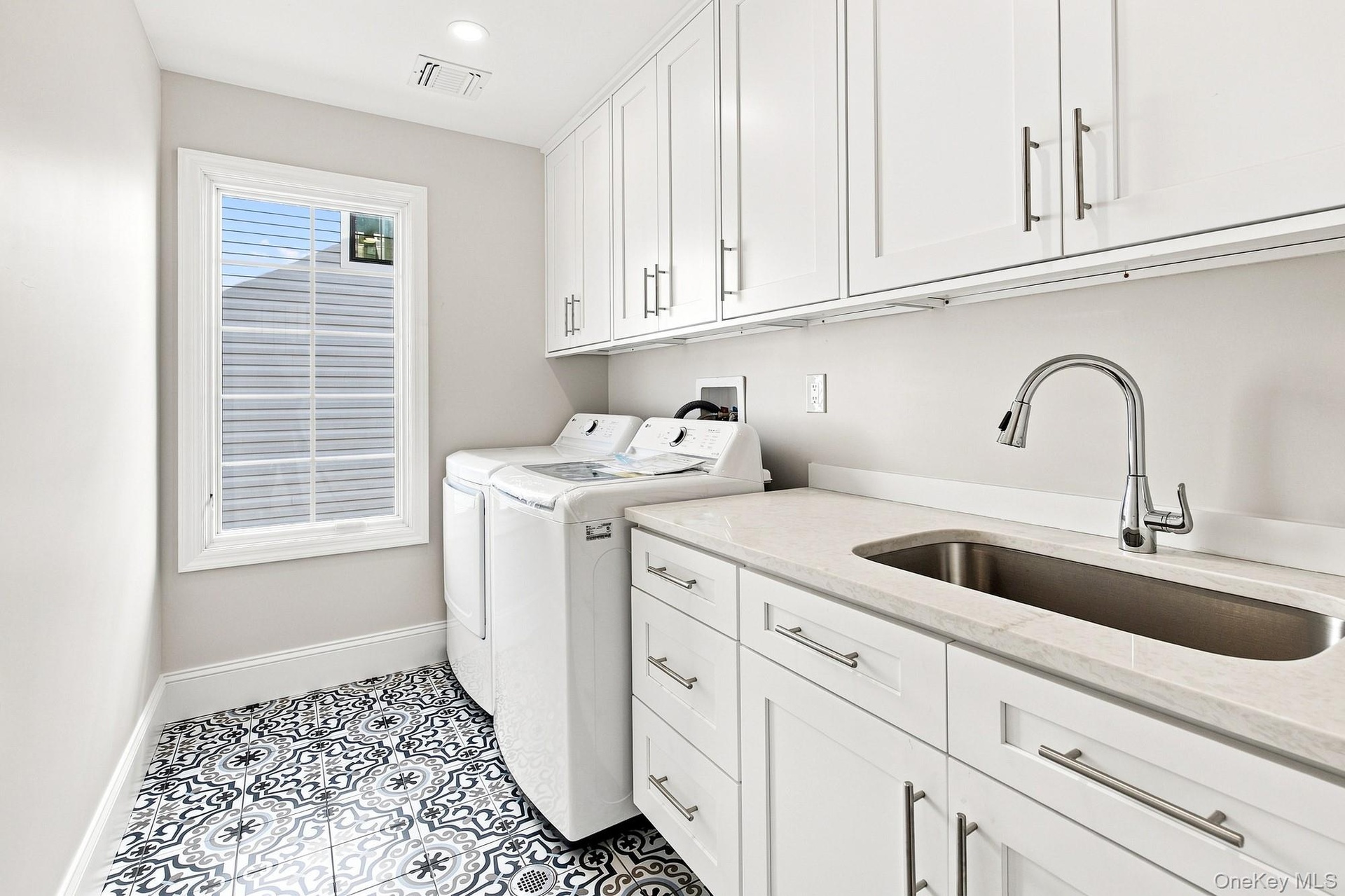 spacious Laundry Room with white shaker-style cabinetry with brushed nickel hardware, light-toned countertop, under mount stainless steel sink with go