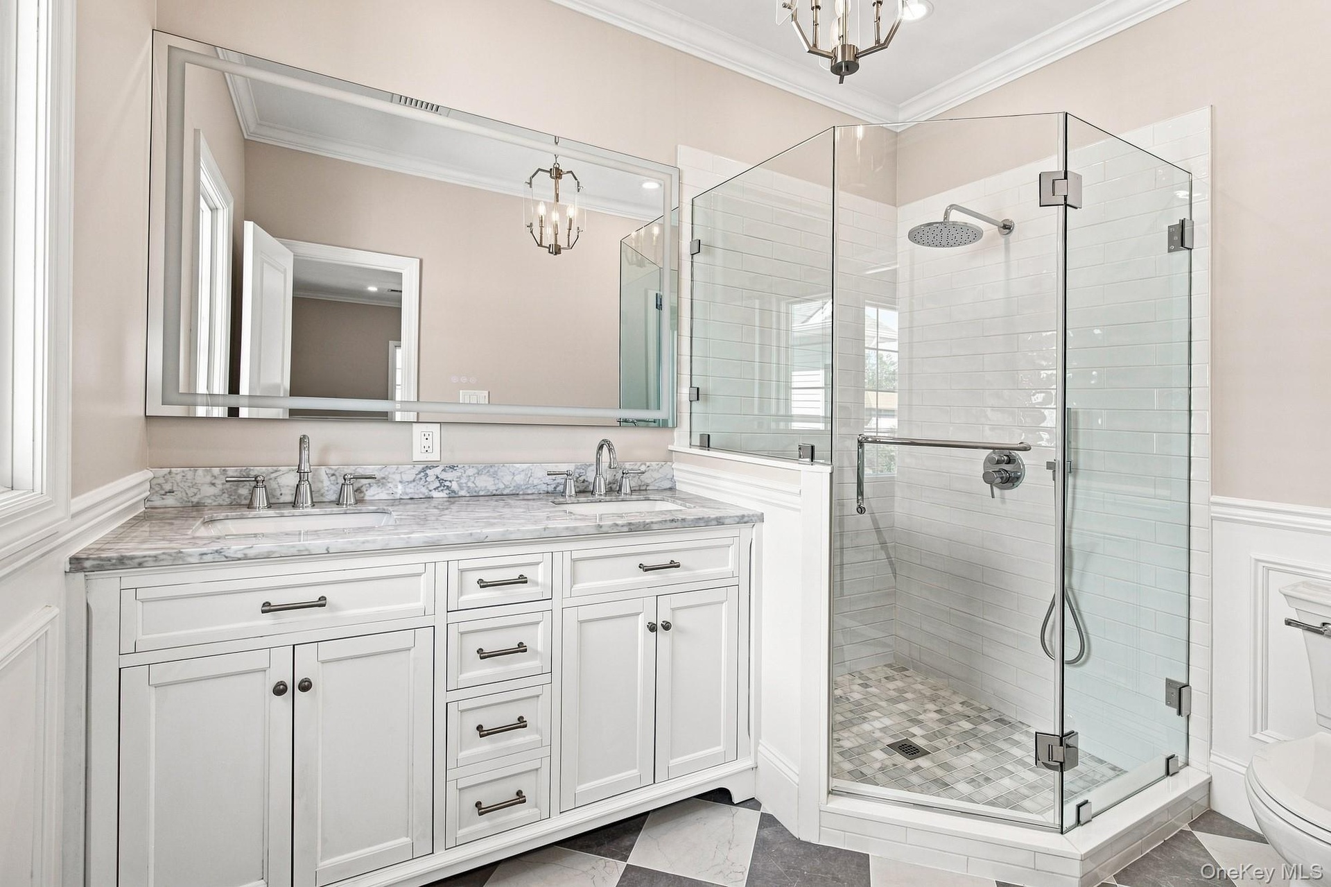 Dual vanity with under mount sinks, stone countertop, and an expansive mirror, large shower.