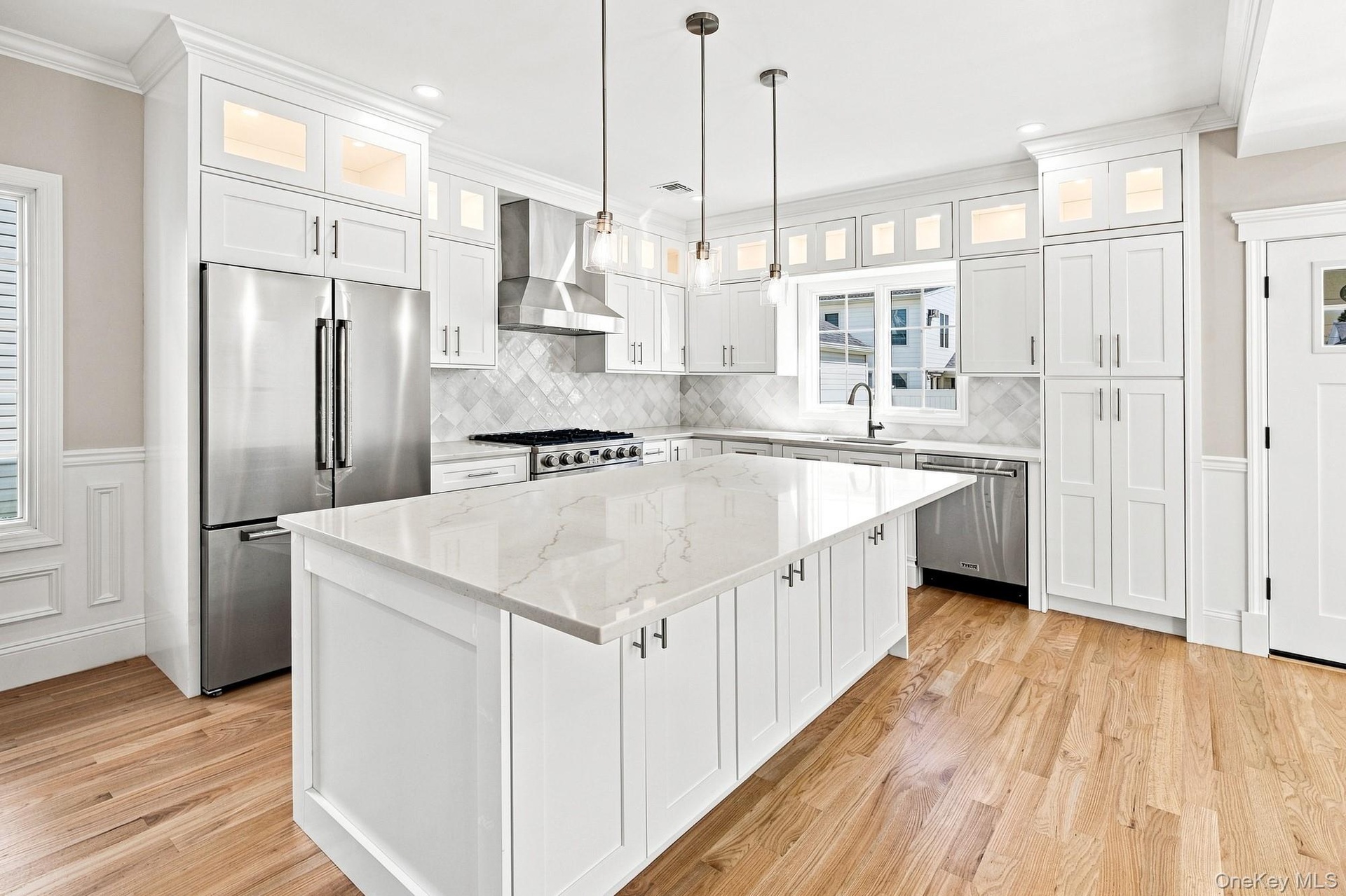 Gourmet Kitchen with a large center island featuring a white quartz countertop, stainless steel appliances, white shaker cabinetry, and wood-finish fl
