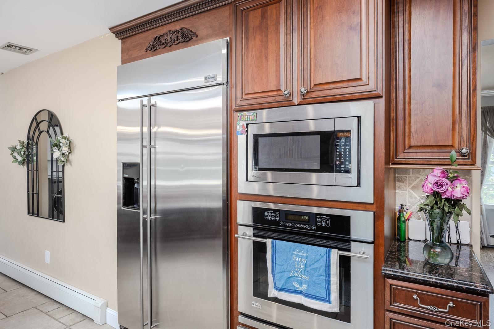 Stainless steel refrigerator, integrated microwave, built-in oven, wood cabinetry, and dark countertop