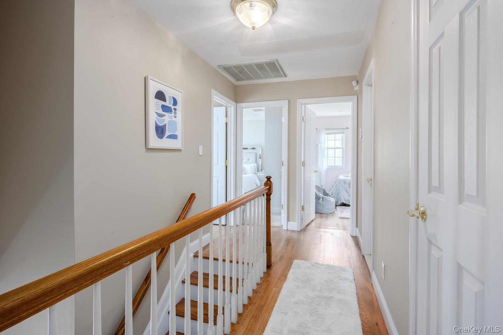 Hardwood flooring throughout the hallway and staircase, featuring white risers and a wood-finish handrail