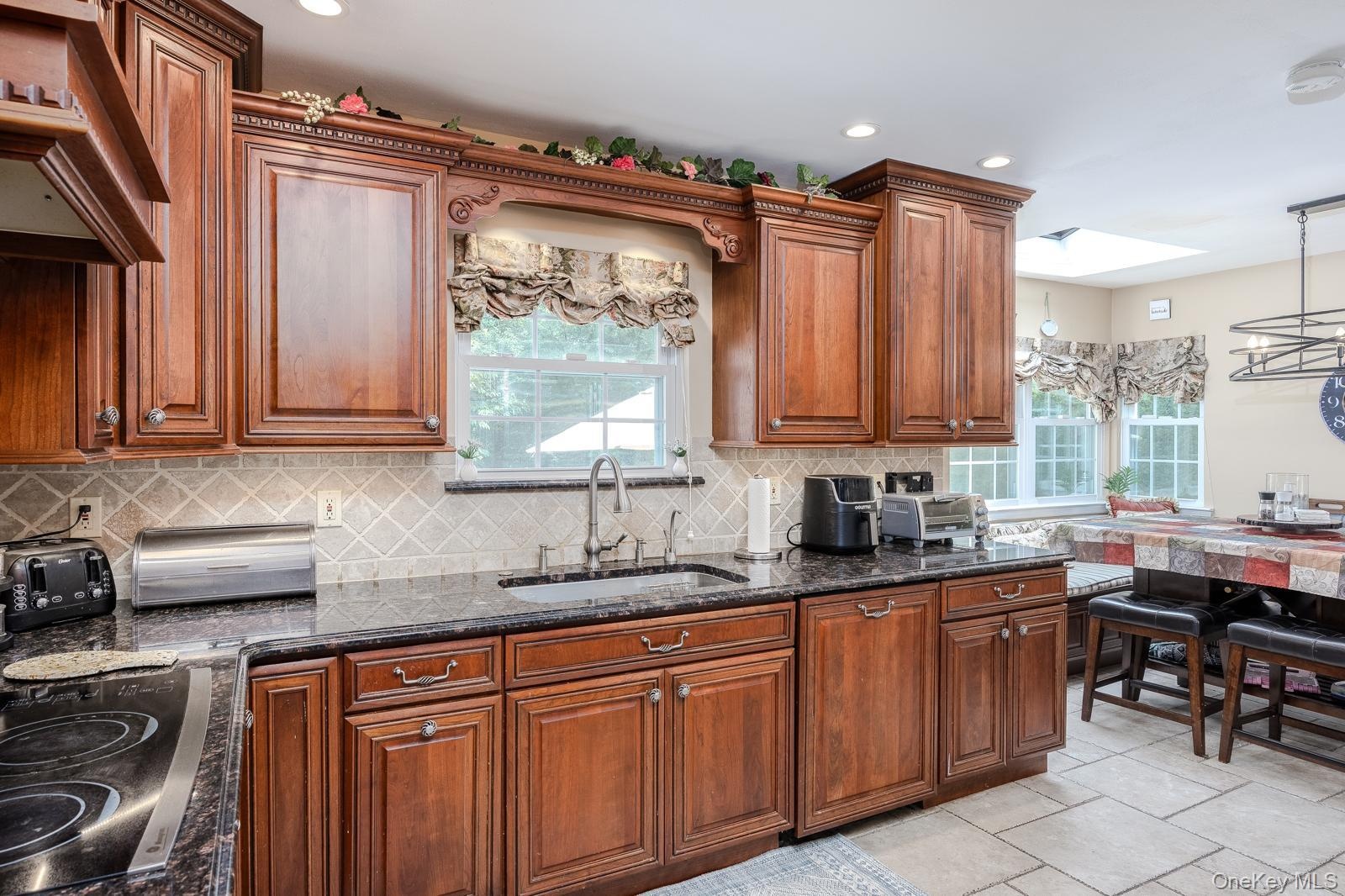 Rich wood cabinetry with decorative molding, dark stone countertops, diamond-patterned tile backsplash, and a contemporary sink faucet