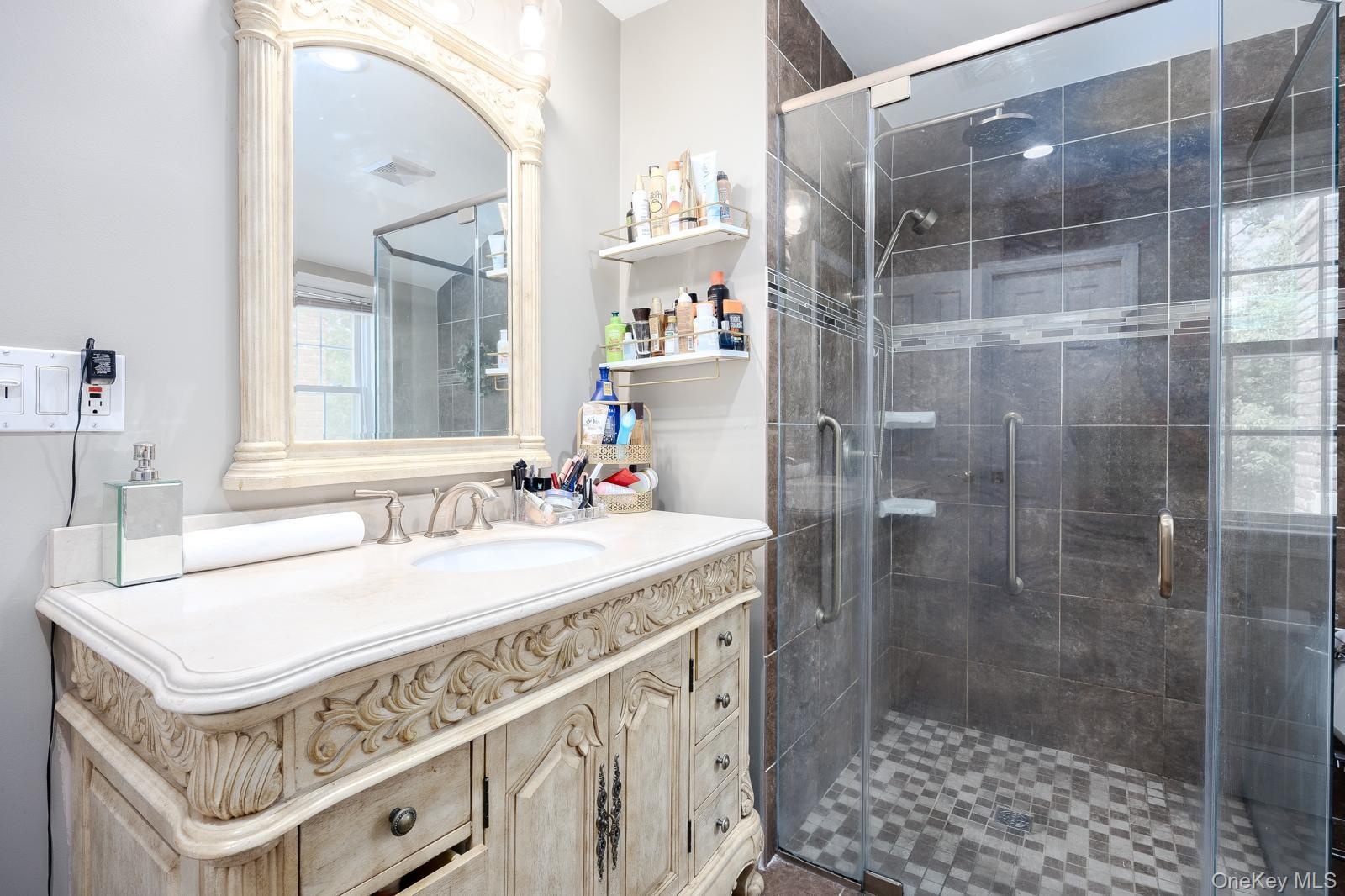 Vanity with an integrated sink, a large framed mirror, and a glass-enclosed shower with tile surround