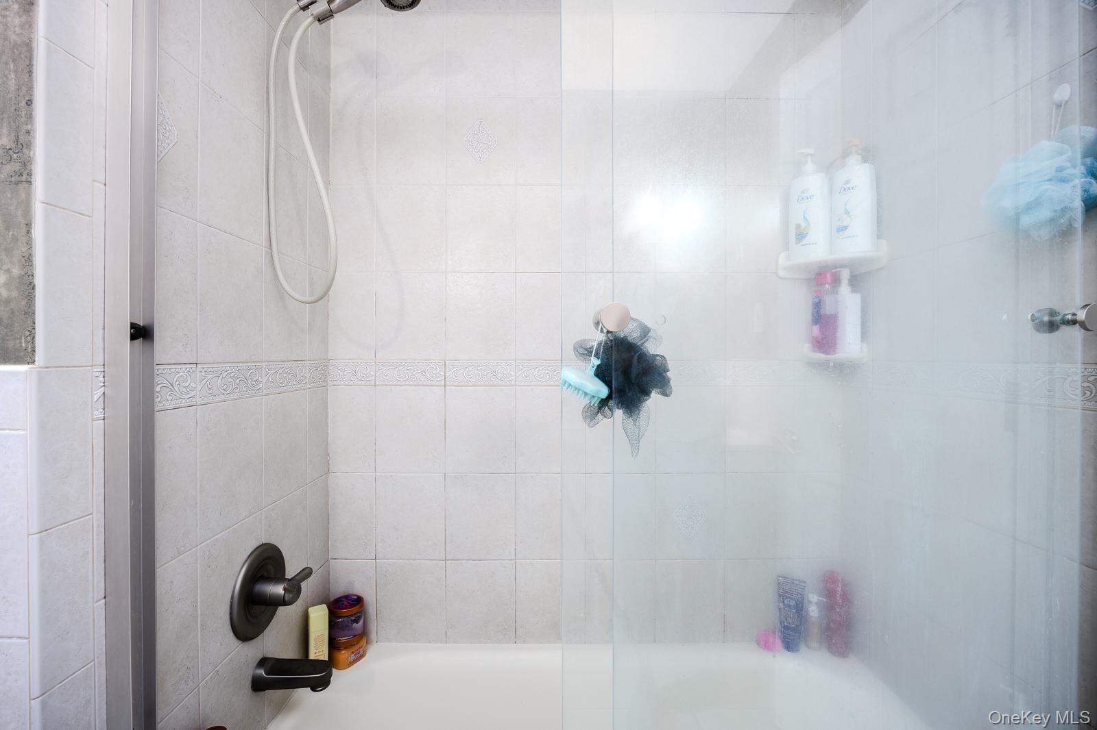 Tub-shower combination featuring white tile surround with  brushed nickel fixtures