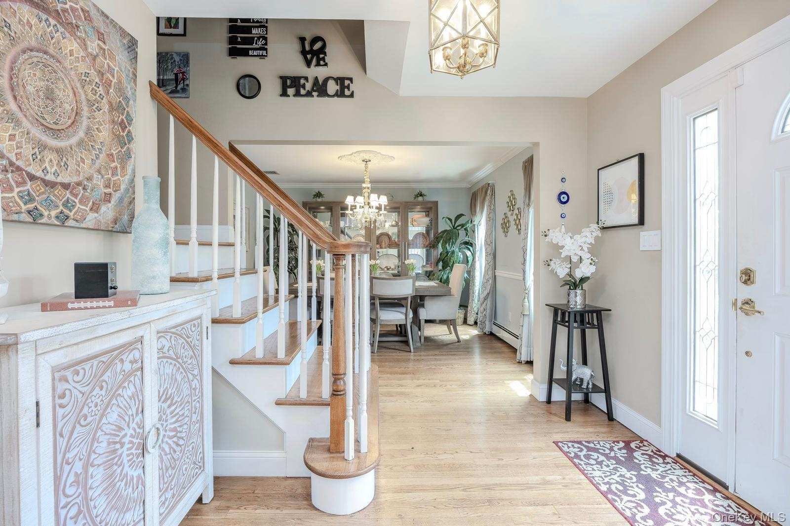 Hardwood flooring throughout, white painted staircase with wood handrail, traditional chandelier lighting, and a white entry door with decorative glas