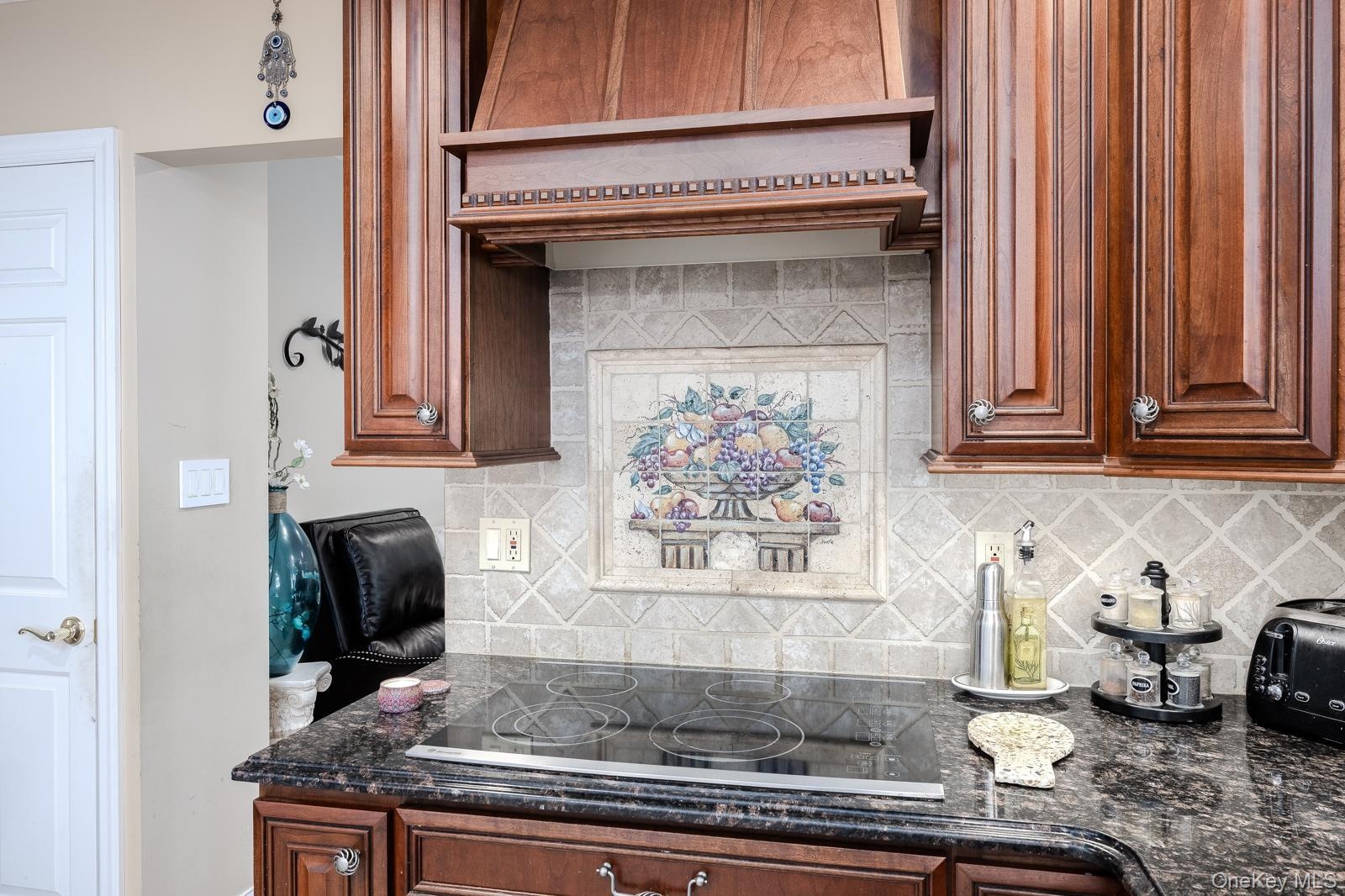 Integrated cooktop with a dark stone countertop, complemented by a decorative tile backsplash and custom wood cabinetry