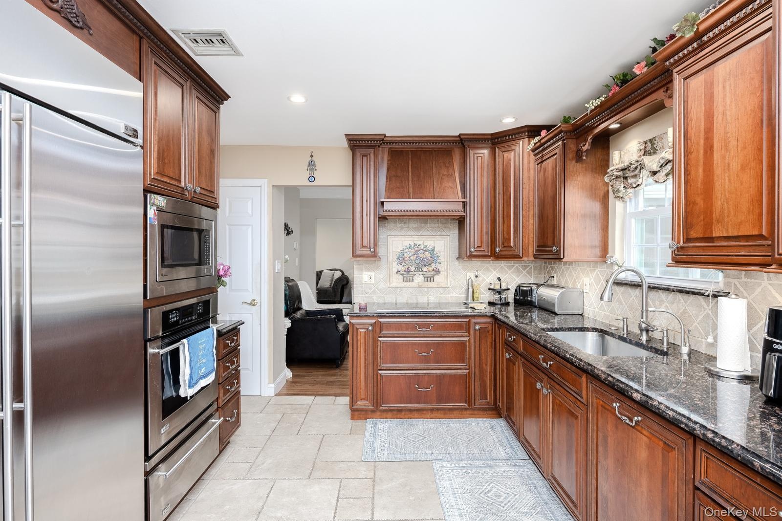 Warm wood cabinetry with crown molding, stainless steel appliances, dark stone countertops, tile backsplash, and a stainless steel sink with a goosene