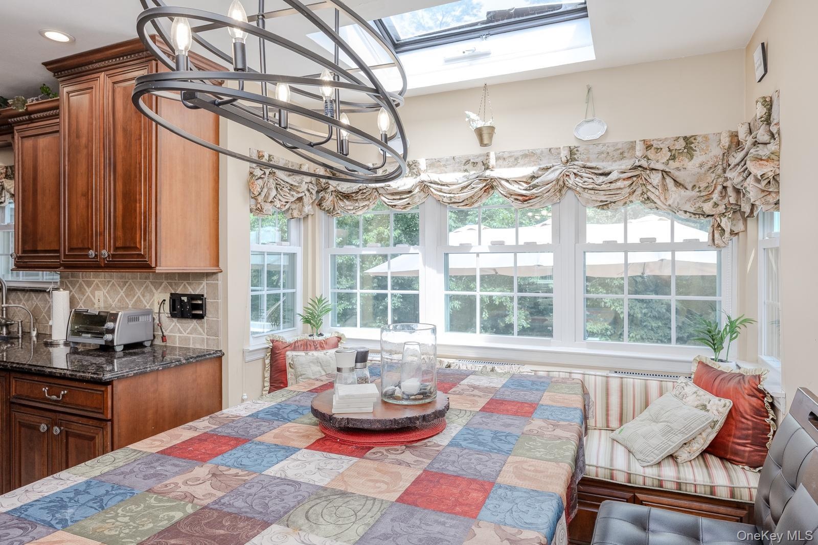 Built-in banquette seating with striped cushions, wood-finish cabinetry, dark stone countertops, skylight, and a decorative overhead light fixture
