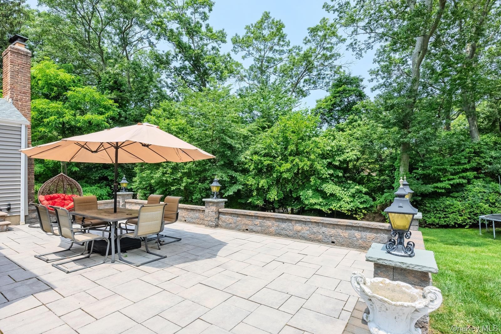 Expansive paver patio with a stone retaining wall and lush perimeter landscaping