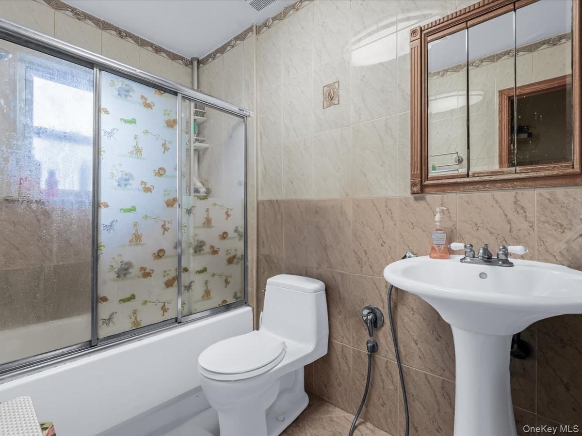 Full bath with bath / shower combo with glass door and tile walls