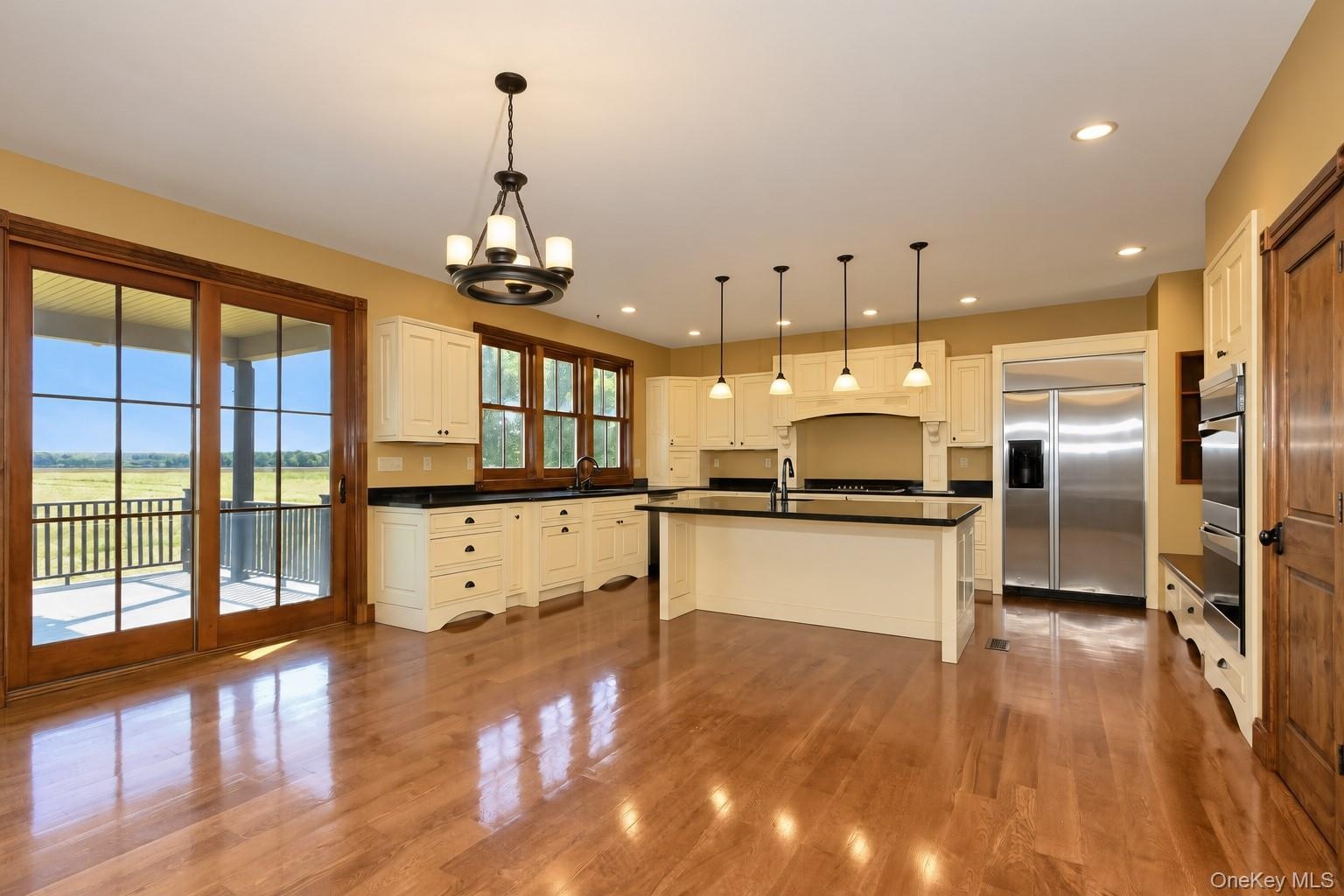 Wood-finish flooring, cream cabinetry, a central island with a dark countertop, stainless steel refrigerator, and double wall ovens