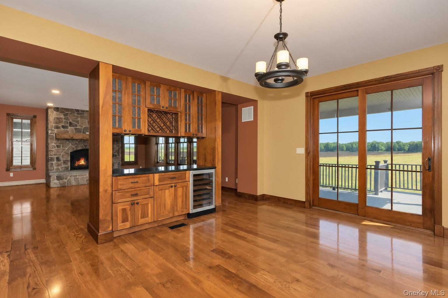 Wood-finish flooring, built-in cabinetry with glass doors, integrated beverage refrigerator, stone fireplace, and sliding glass doors to outdoor space