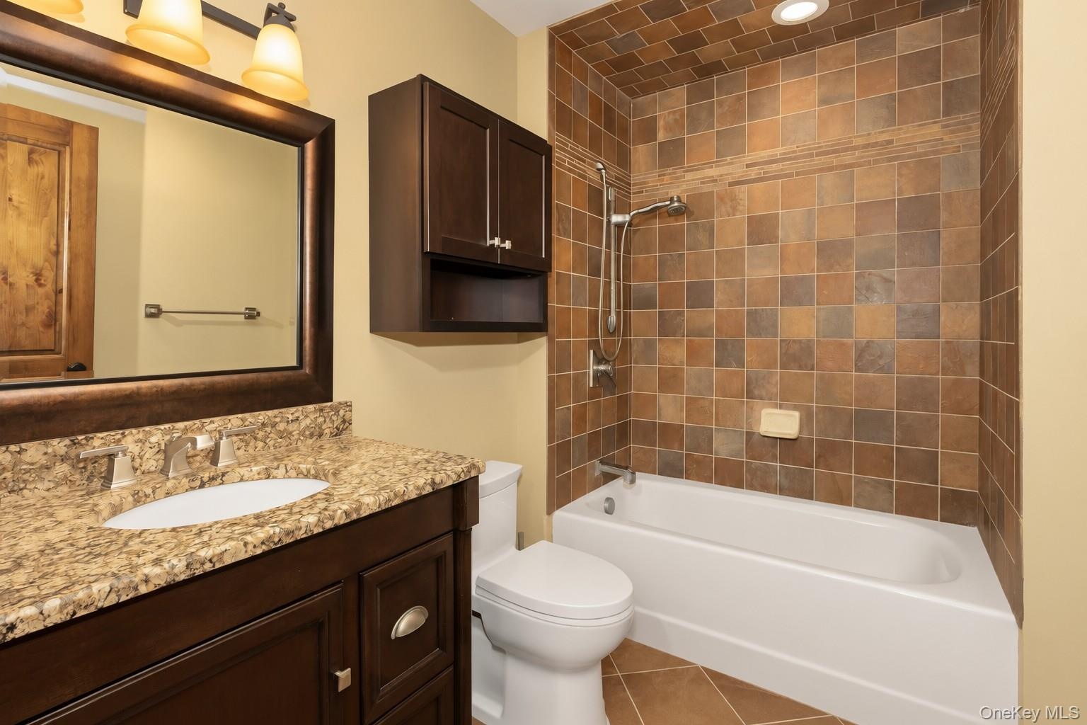 Vanity with granite countertop and undermount sink, framed mirror, wall-mounted storage cabinet, and a tiled shower/tub combination