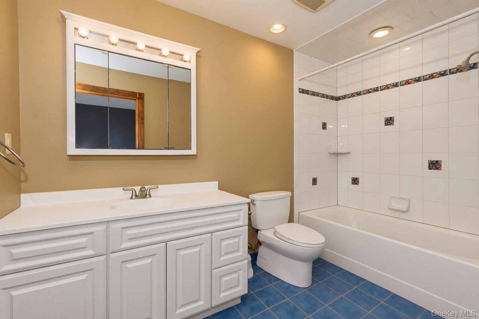Built-in vanity with white cabinetry and integrated sink, mirrored medicine cabinet with vanity lighting, tiled shower and bathtub combination, and bl
