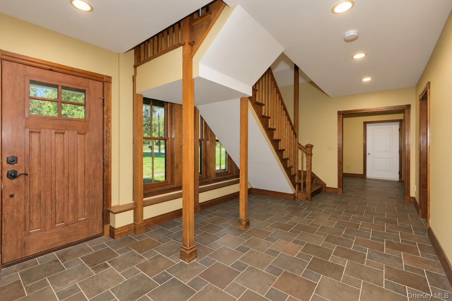 Foyer featuring tile flooring, a solid wood entry door with glass panels, wood-framed windows, a wood staircase, and recessed lighting