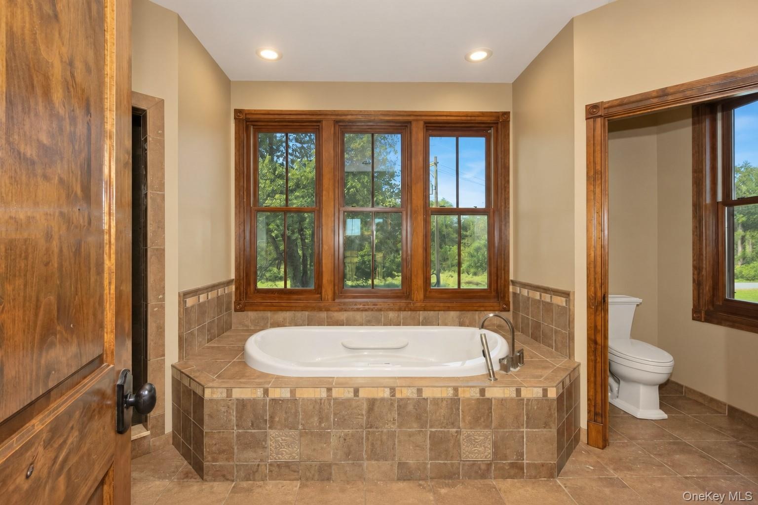 Soaking tub with tile surround, wood-framed windows, and recessed lighting