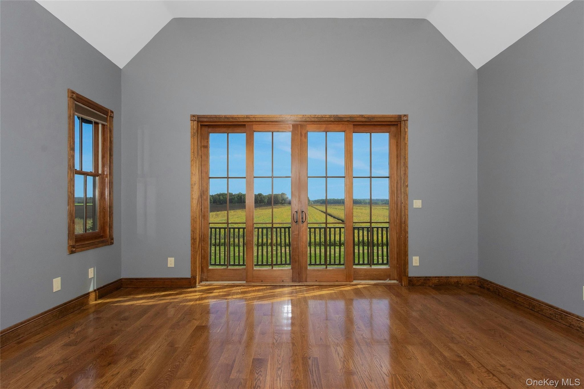 Vaulted ceiling, wood-finish flooring, full-light French doors with wood trim, wood-trimmed window, and balcony with black railing