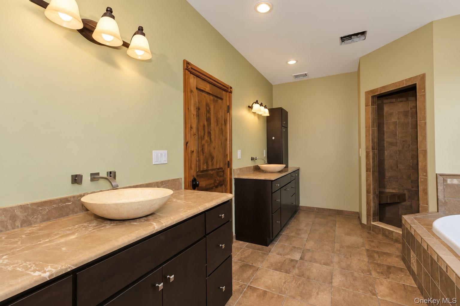 Dual vanity with vessel sinks, wall-mounted faucets, and stone countertops