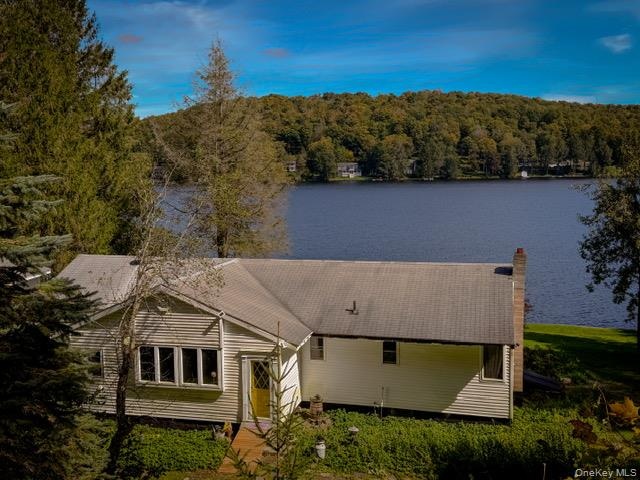 Lakefront property with mature trees, a shingled roof, and a prominent chimney