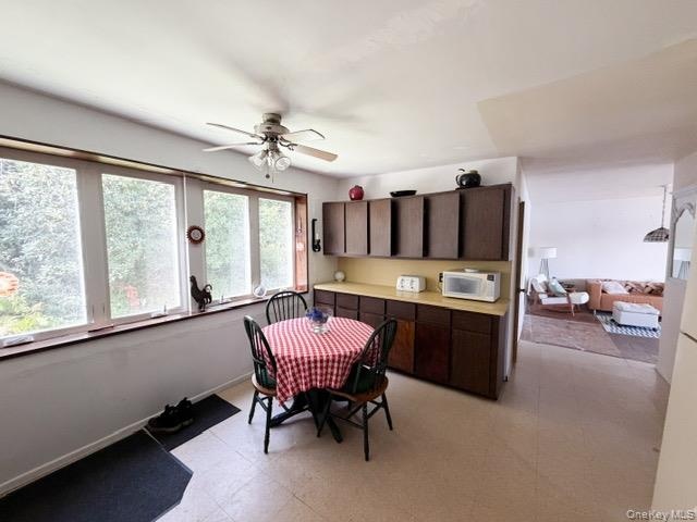 Kitchen area featuring a ceiling fan with integrated lighting, wood-finish cabinetry, a light-toned countertop, and expansive windows