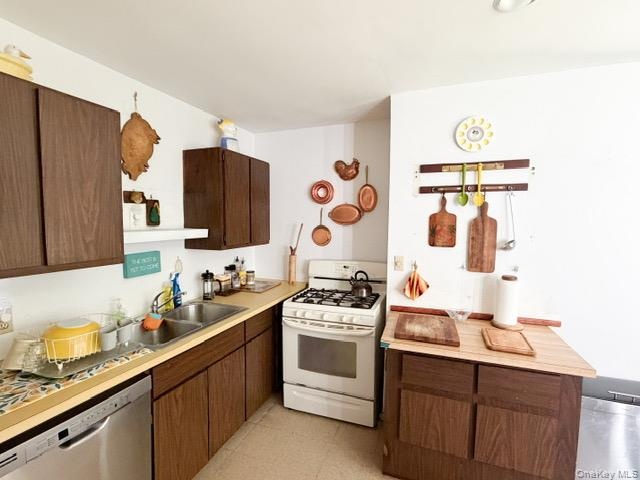 Kitchen featuring wood-finish cabinetry, a stainless steel double basin sink, and a white gas range