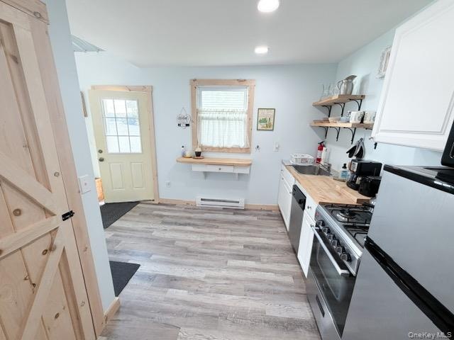 Wood-finish flooring throughout, stainless steel gas range, wooden open shelving, light wood countertops, and a full-light panel door