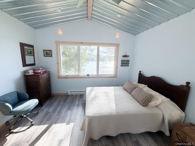 Vaulted metal ceiling with exposed wood beams, large window with wood trim, and wood-finish flooring