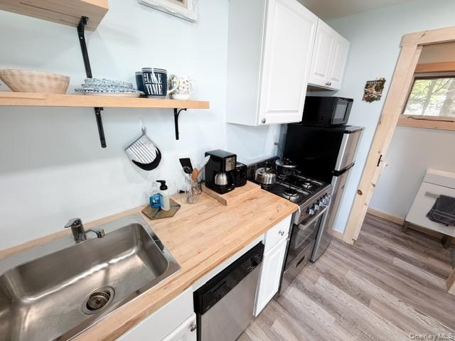 Compact kitchen featuring wood-finish countertops, a stainless steel sink, a dishwasher, a freestanding range, and upper cabinetry