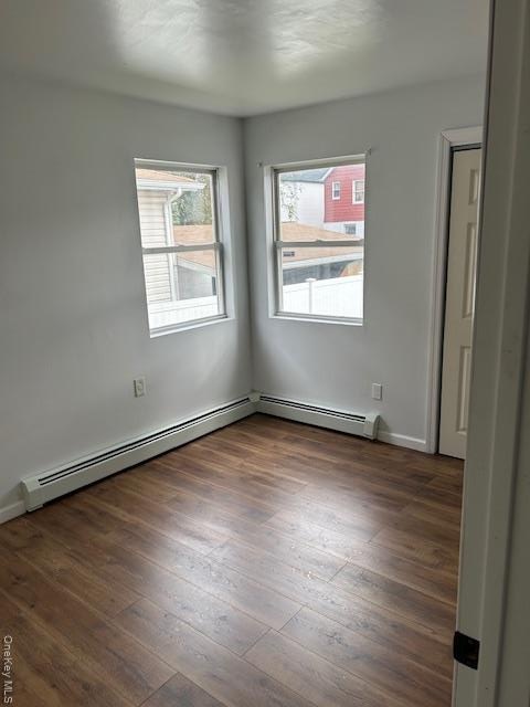 Spare room featuring plenty of natural light, dark wood-style floors, and a baseboard heating unit