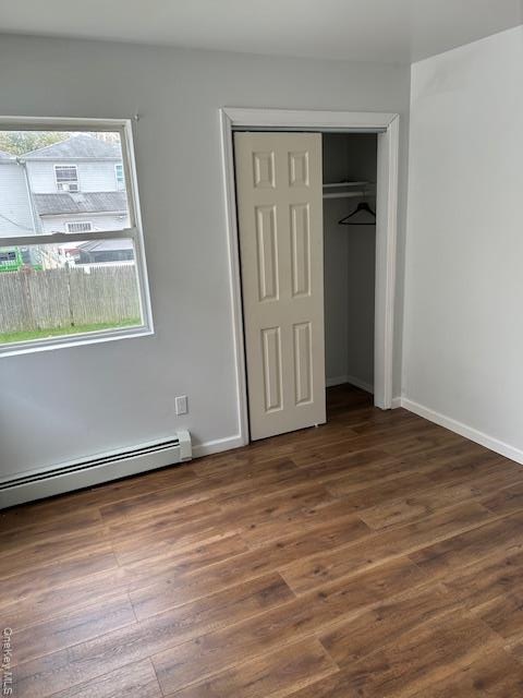 Unfurnished bedroom featuring a baseboard heating unit, dark wood-style floors, and a closet