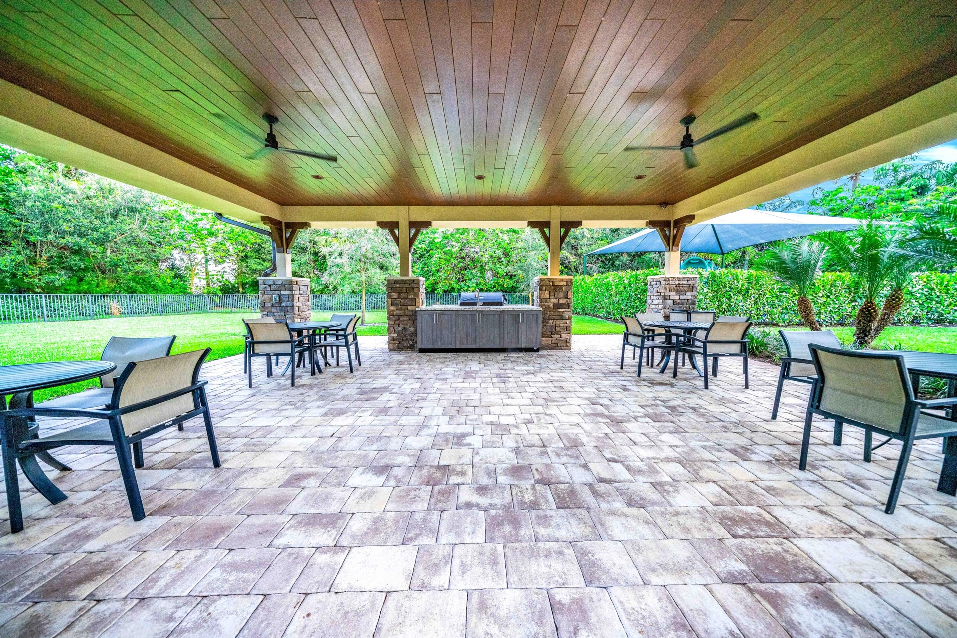 Expansive covered patio featuring a wood-finish ceiling, paver flooring, stone-clad columns, built-in grill station, and integrated ceiling fans