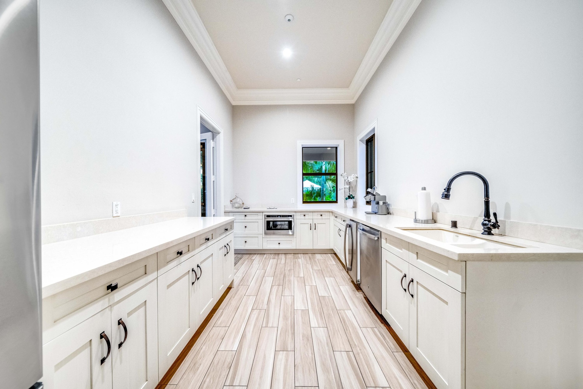 Expansive kitchen featuring wood-finish flooring, white cabinetry with dark hardware, light-toned countertops, a stainless steel dishwasher, and a dee