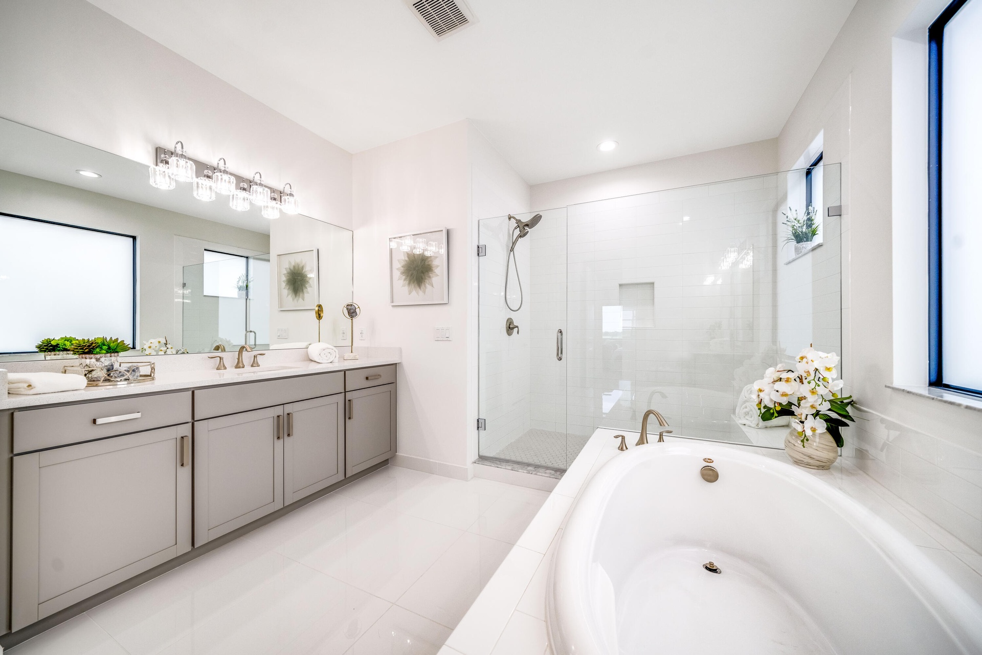 Dual vanity with undermount sinks, a built-in soaking tub, a glass-enclosed shower, and large format floor tiling