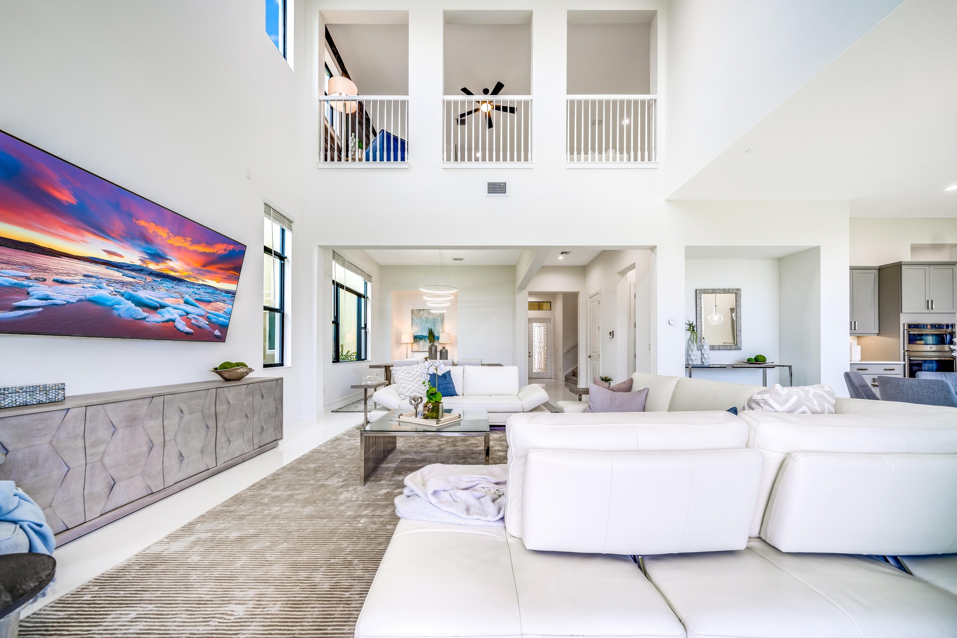 Soaring ceilings with upper-level balconies, expansive windows, recessed lighting, and a contemporary built-in media console
