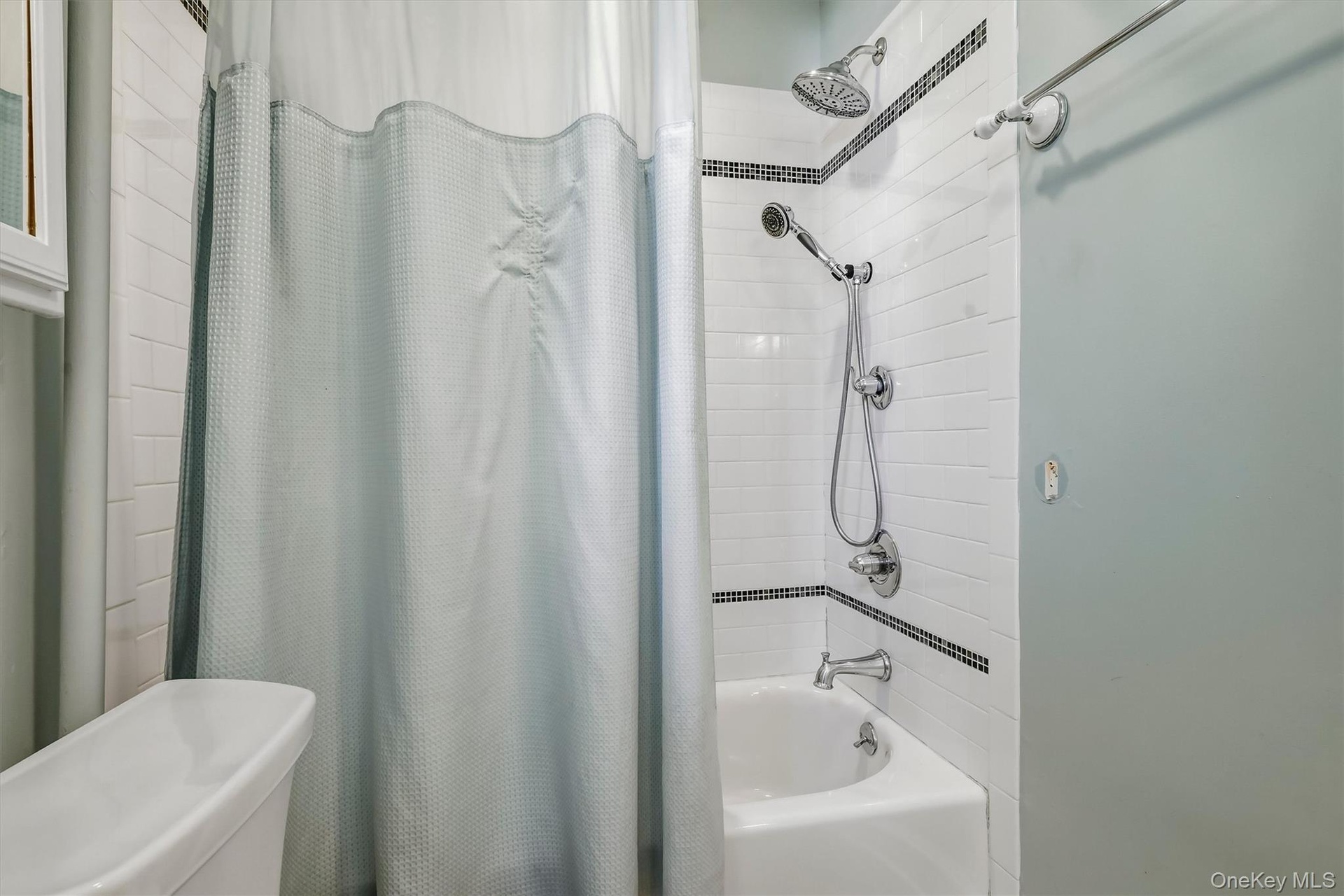 Tub and shower combination with subway tile surround, decorative tile accent, and a dual-function shower head