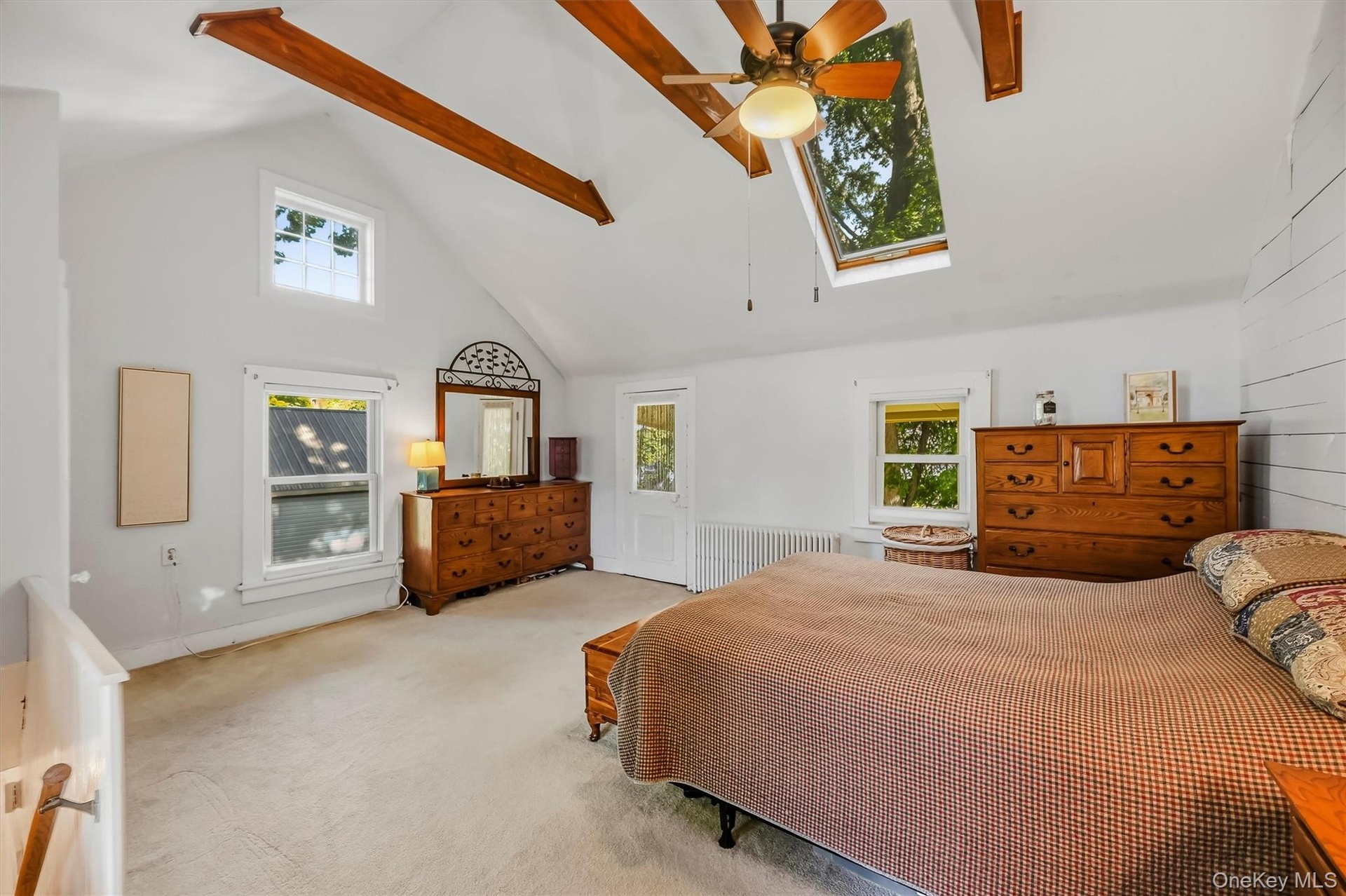 Spacious primary bedroom with vaulted ceiling, exposed wood beams, skylights, and abundant natural light