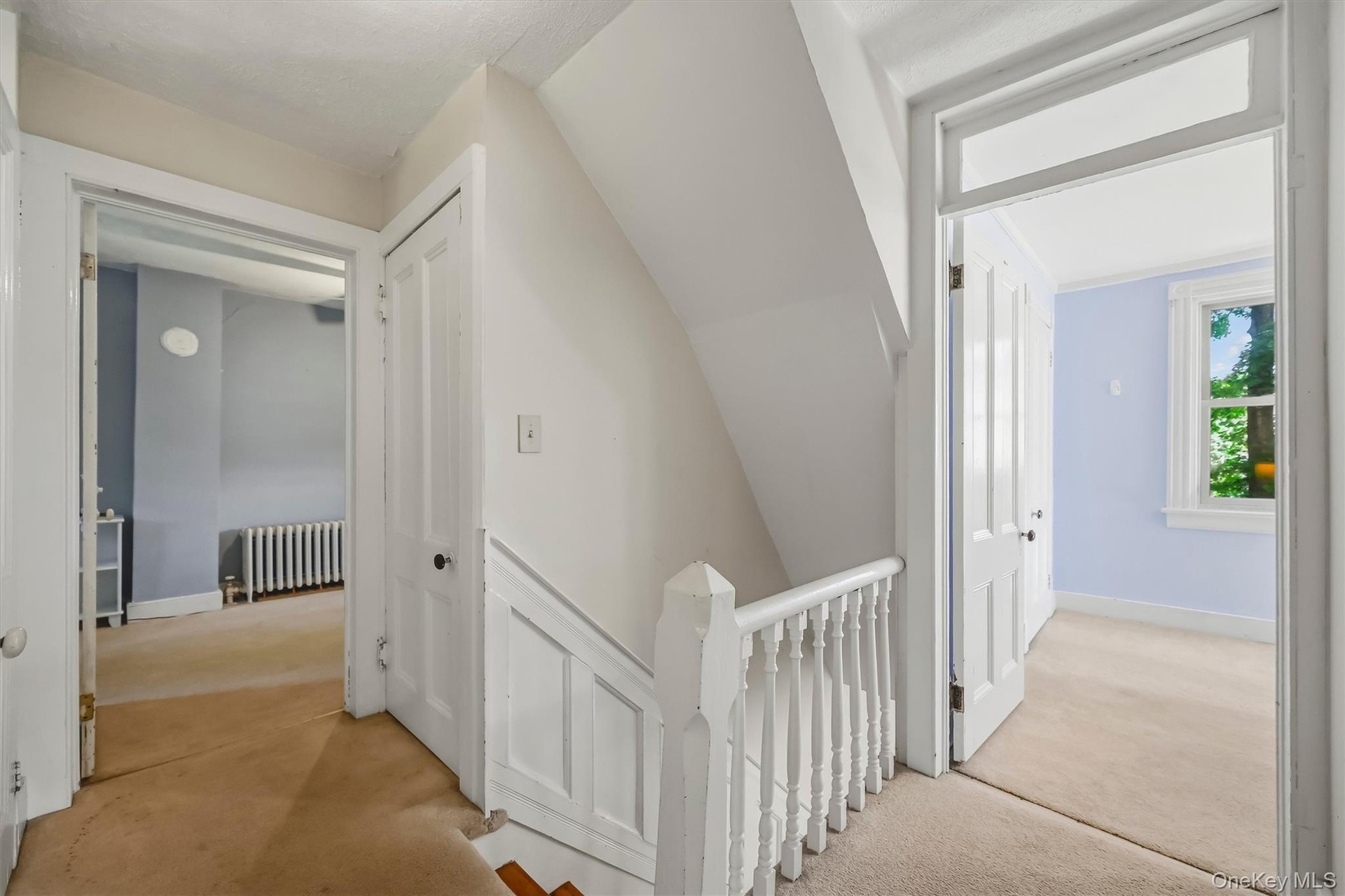 Carpeted hallway with white painted balusters and railings, featuring two paneled doors and a window with white trim