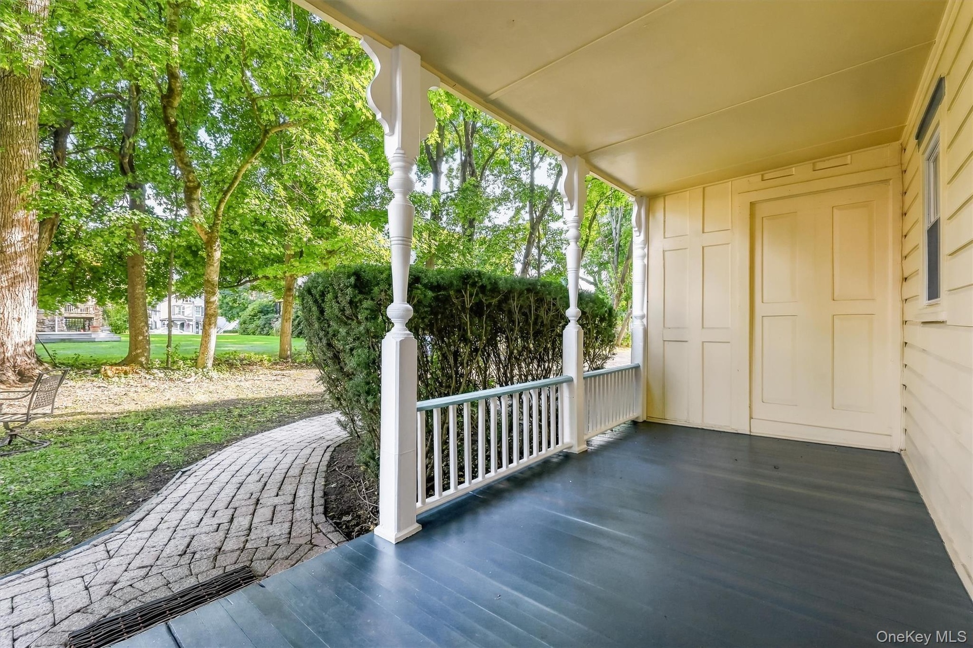 Covered porch with decorative columns, painted wood flooring, and paneling along the exterior wall