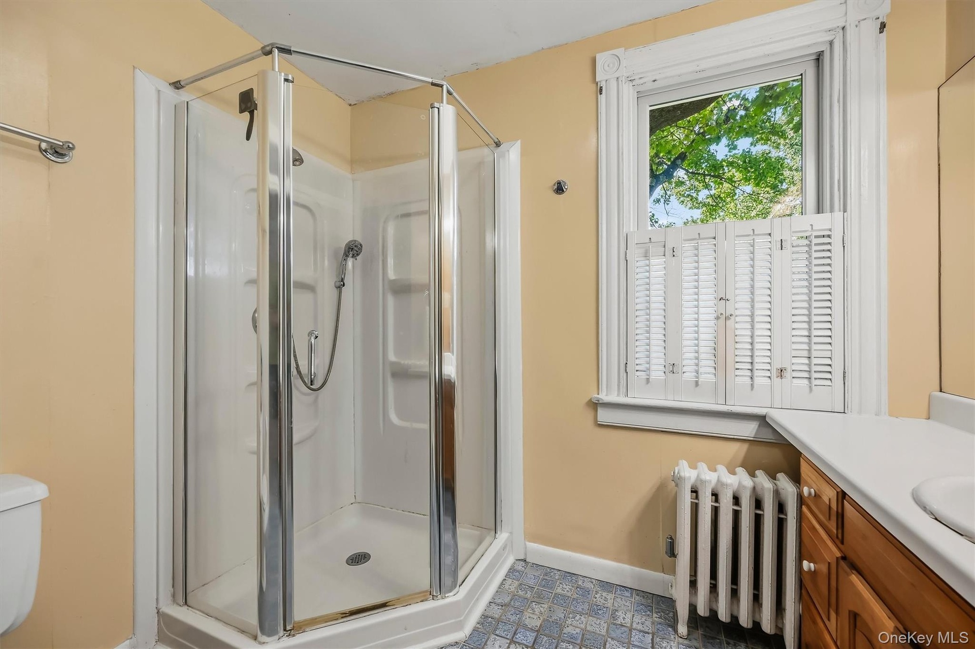 Corner shower enclosure with glass panels, white window shutters, and a wood-finish vanity with an integrated sink