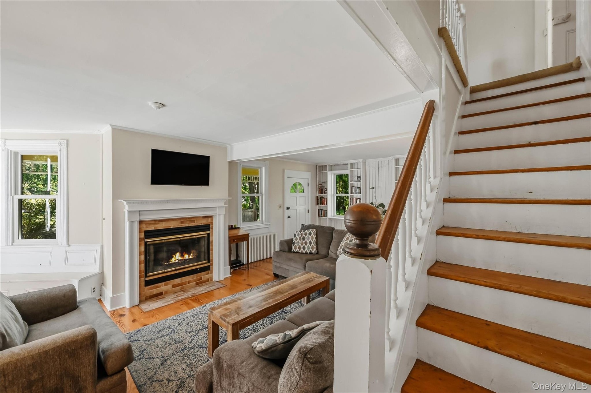 Hardwood flooring, brick fireplace with a white mantel, white trim, recessed lighting, and a detailed staircase with a wood handrail
