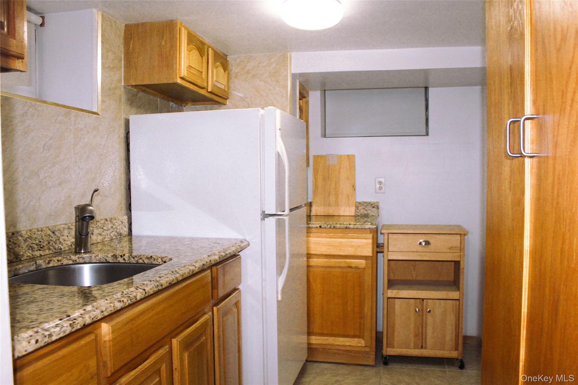 Wood-finish cabinetry with a built-in stainless steel sink, granite-style countertops, and a full-size refrigerator