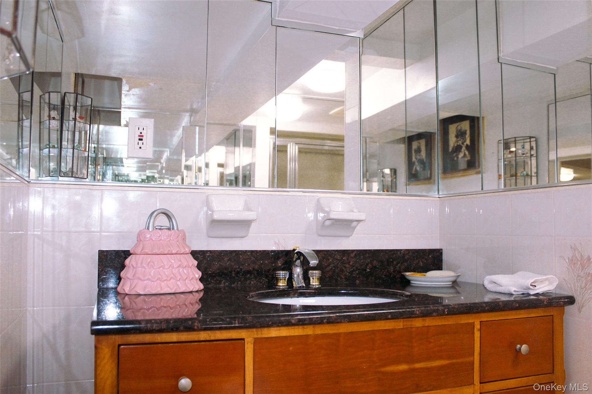 Basement bathroom with wood-finish vanity with drawer storage, dark stone-finish countertop, and a built-in sink basin