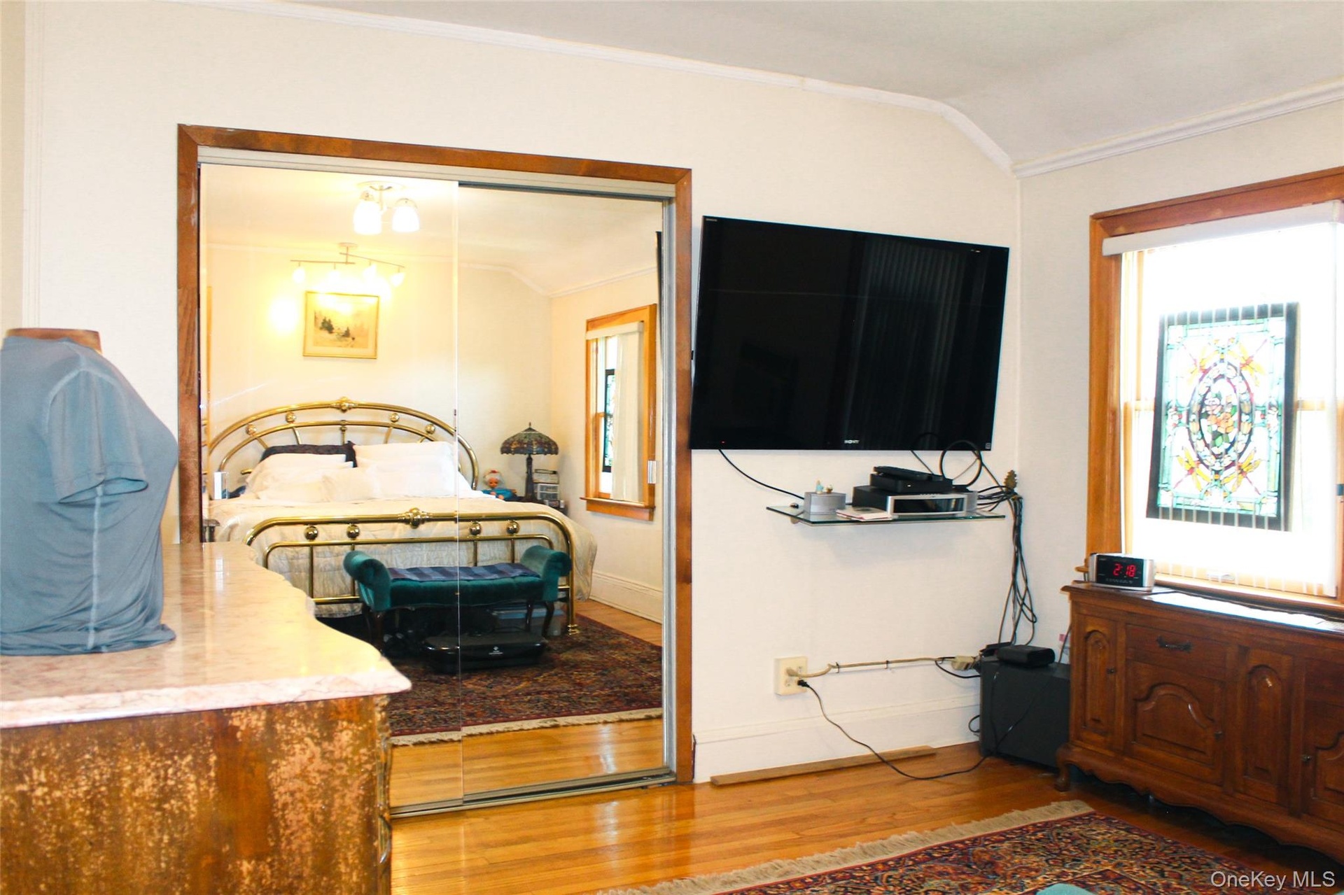 Bedroom 1 has hardwood flooring, crown molding, and a stained glass window detail with large closet