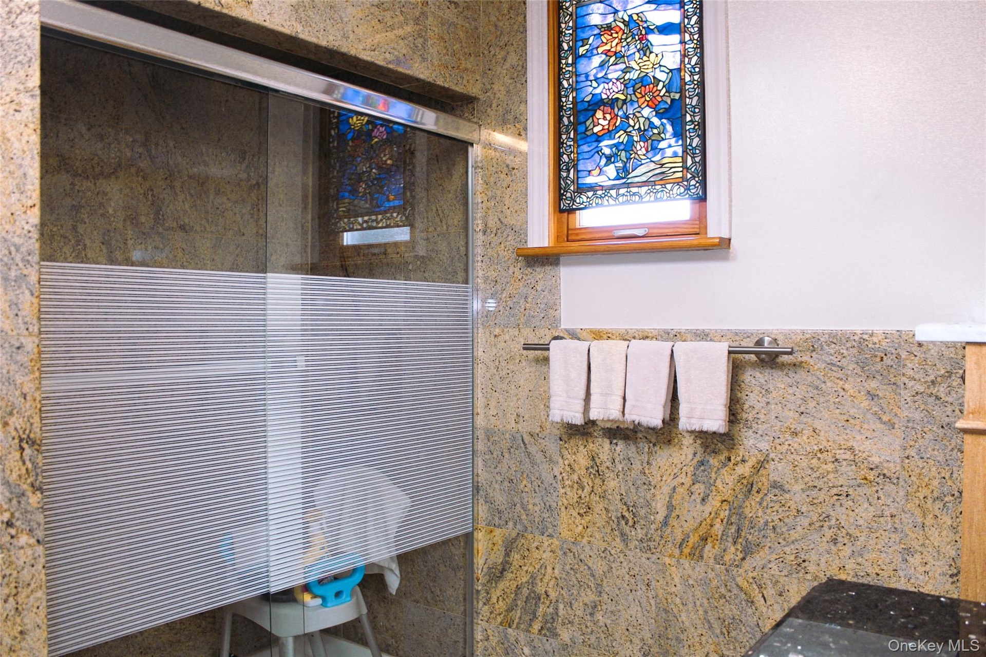 2nd floor bathroom has glass-enclosed shower with frosted panel, natural stone wall finishes, and a stained-glass window accent
