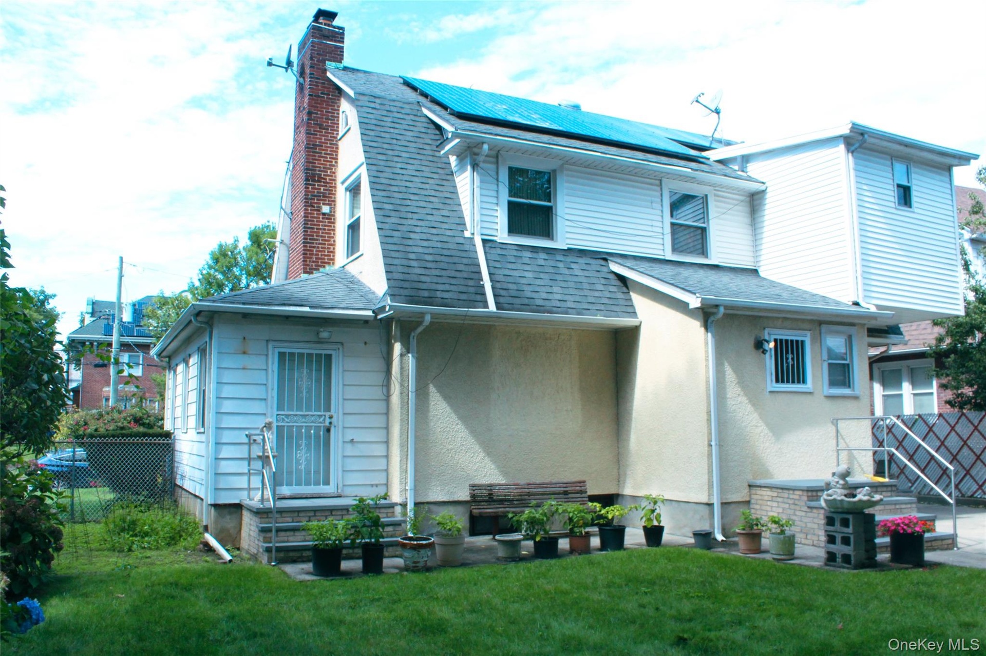 Manicured lawn, brick chimney, multiple windows, solar panels, and a rear entry door