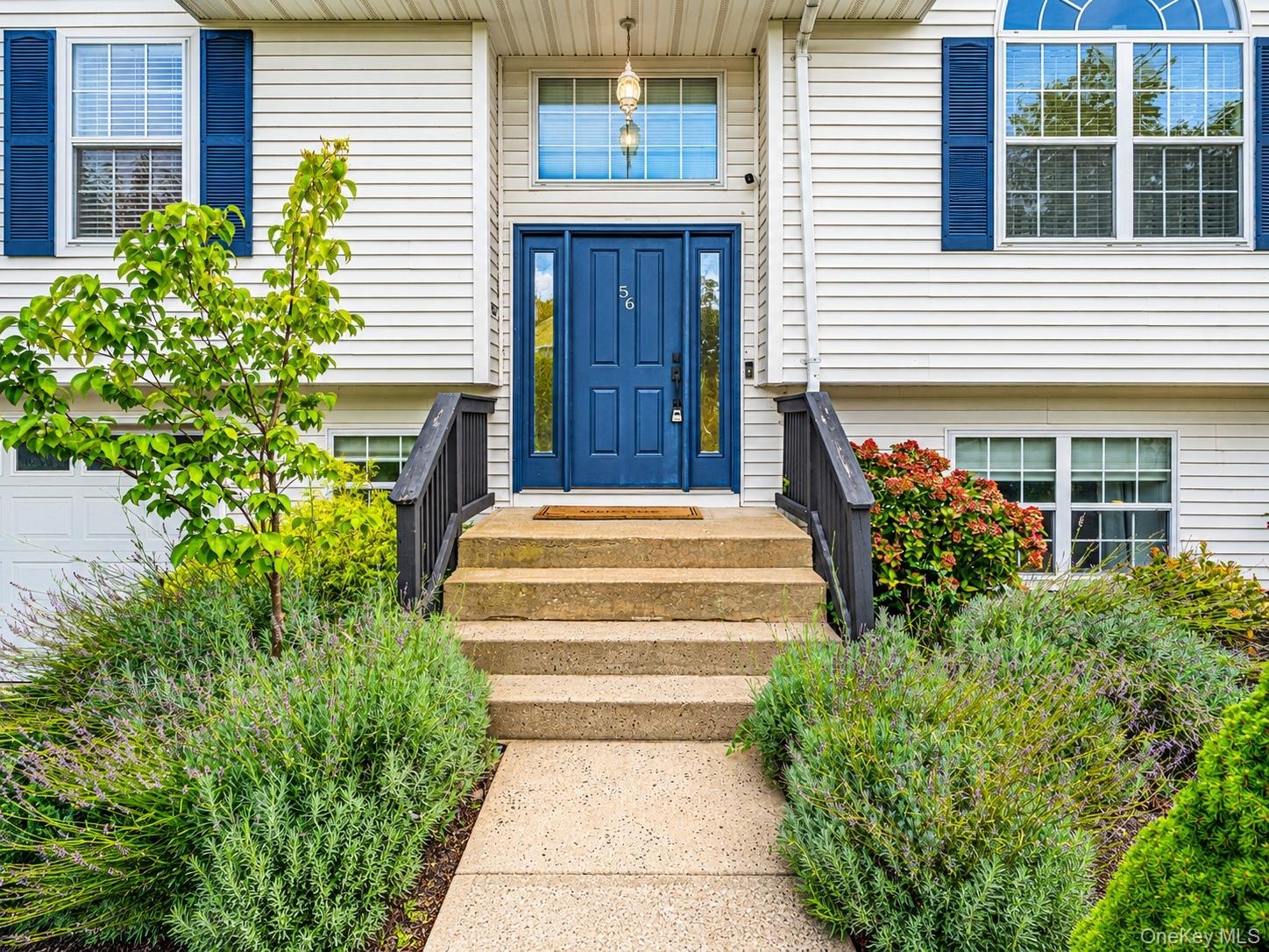 White siding exterior with a prominent blue entry door, complementary blue window shutters, an arched transom window, and a concrete pathway leading t