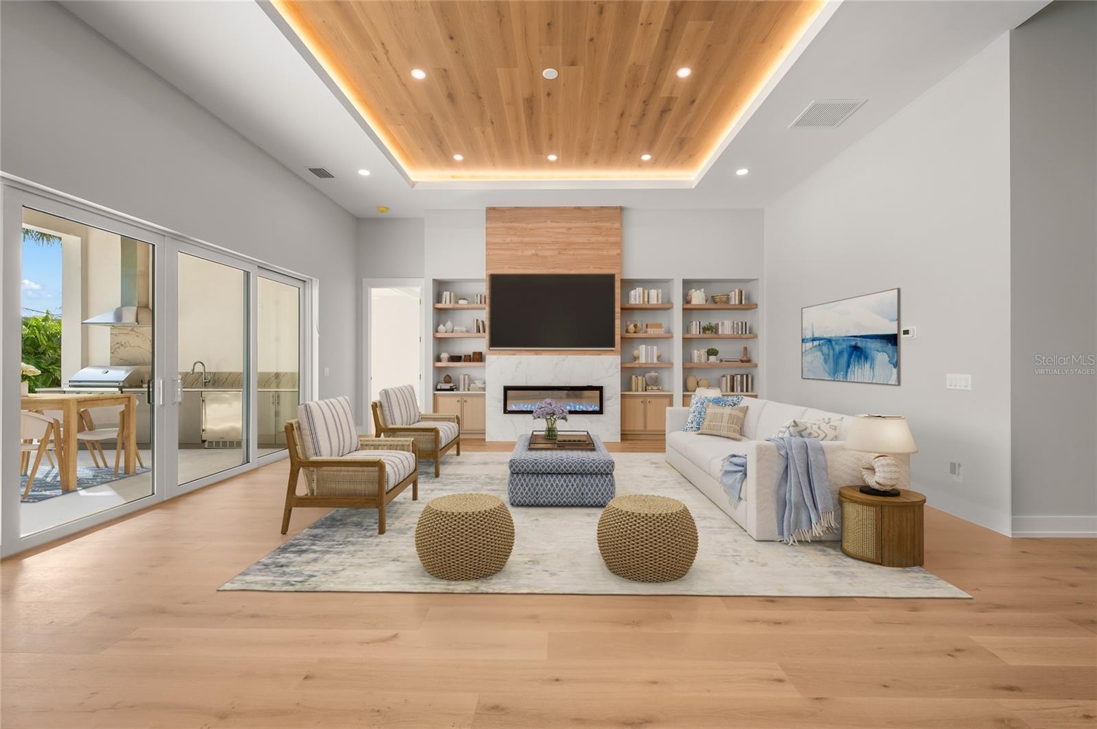 Virtually staged family room featuring a modern fireplace and custom built-ins, opening seamlessly to the outdoor entertaining area.