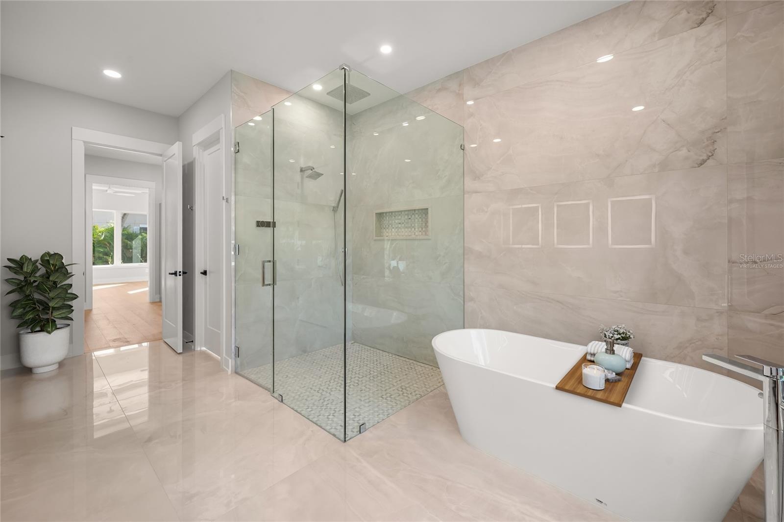 Virtually staged primary suite features a luxurious spa-inspired bath with soaking tub, spacious walk-in shower, designer tile, beautifully curated fi