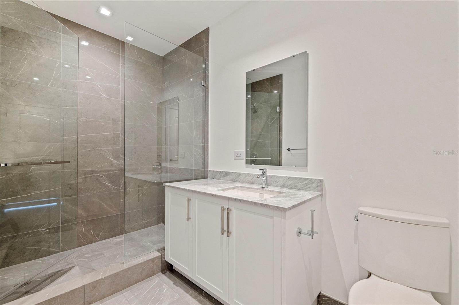 Clean-lined en-suite luxury with marble finishes and a glass-enclosed shower.